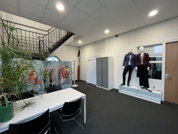 Showroom met twee etalagepoppen in zakelijke kleding, een tafel met stoelen, en promotieborden onder een trap bij Niels Bohrweg.